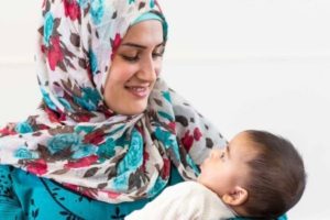 A woman wearing a brightly coloured headscarf looks lovingly at the child she is holding.