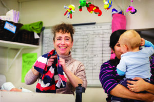 Early-learning-staff-with-child Woman smiling while holding a child's jumper and woman beside her holding a baby