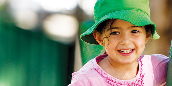 Young girl wearing a green bucket hat and pink t-shirt playing and smiling