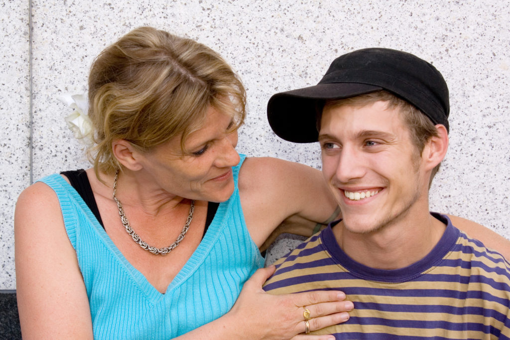 A woman has her arm around a young man wearing a baseball cap.