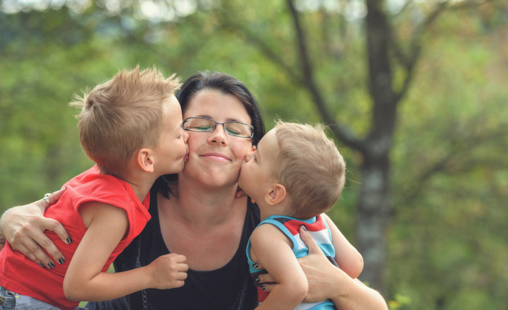 Two young boys kissing their mother on cheek