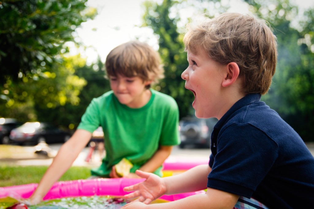 Two boys around the age of 6 and 8 smiling and laughing as they play in a paddling pool
