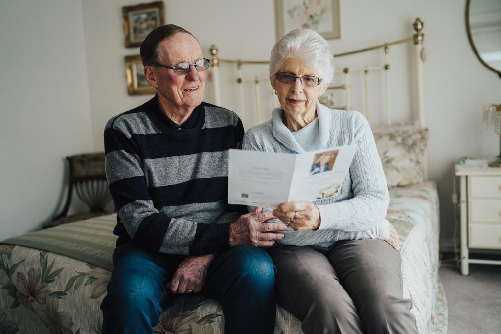 two older people reading a book on a bed