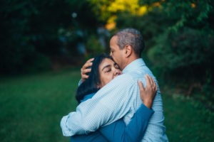 A man and a woman hug in a garden. The man's hand cradles the woman's head